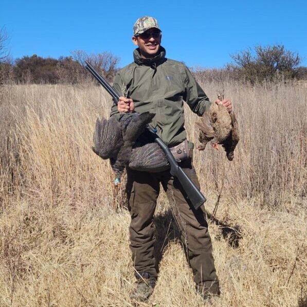 Wingshooter in camouflage holding a shotgun and shot birds in tall grass
