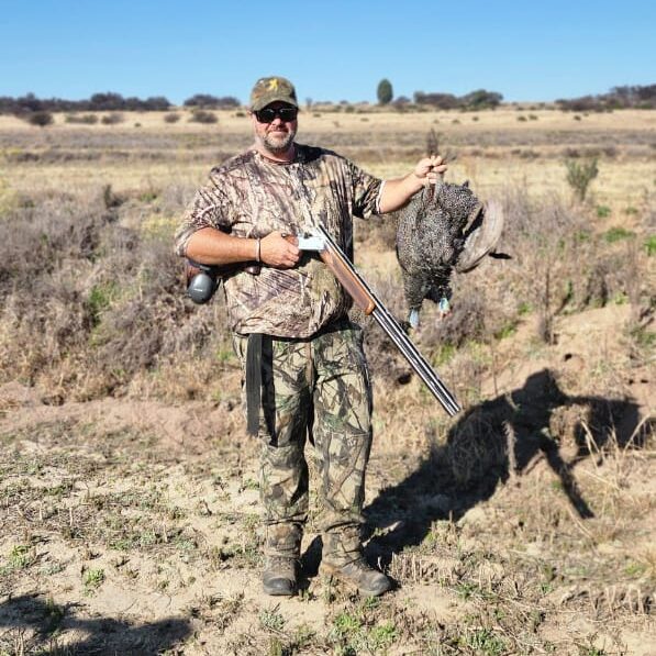 Wingshooter carrying a shotgun and a bag of birds across a field
