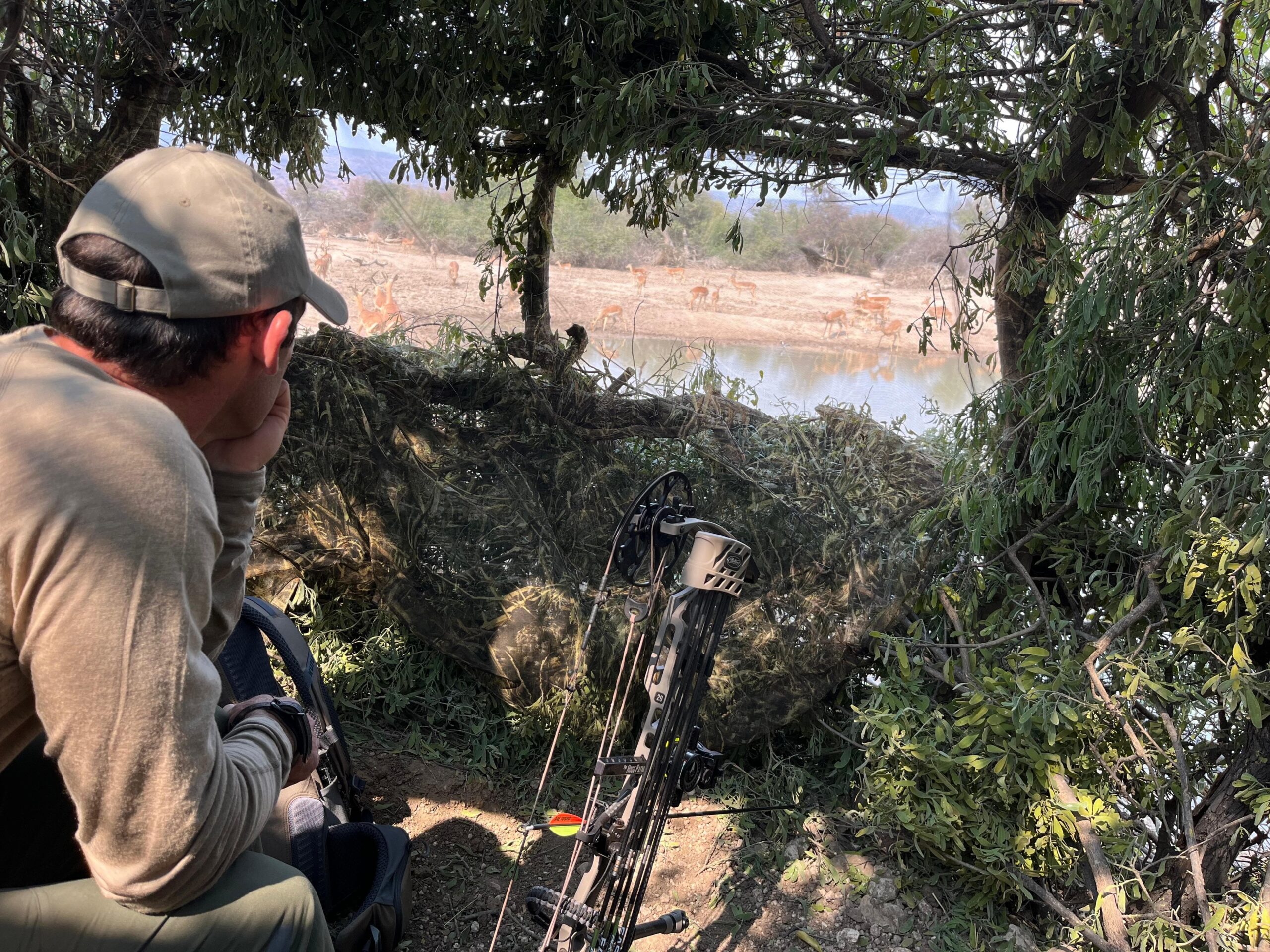 Bow hunter waiting in a brush blind overlooking water