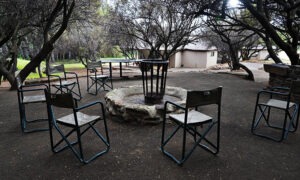 Fire pit surrounded by director's chairs under the trees